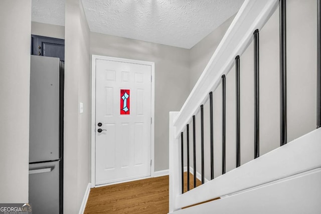 foyer entrance with light wood-style floors, baseboards, and a textured ceiling