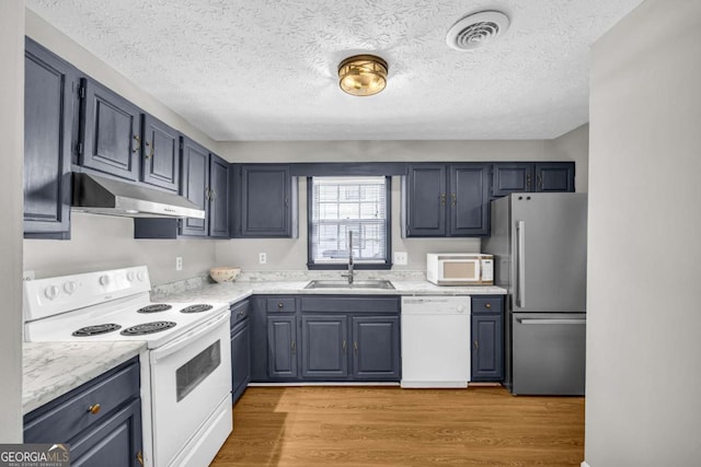 kitchen with white appliances, visible vents, light wood-style flooring, under cabinet range hood, and a sink