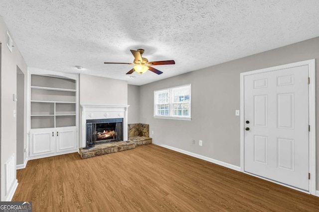 unfurnished living room with baseboards, a ceiling fan, wood finished floors, a lit fireplace, and a textured ceiling