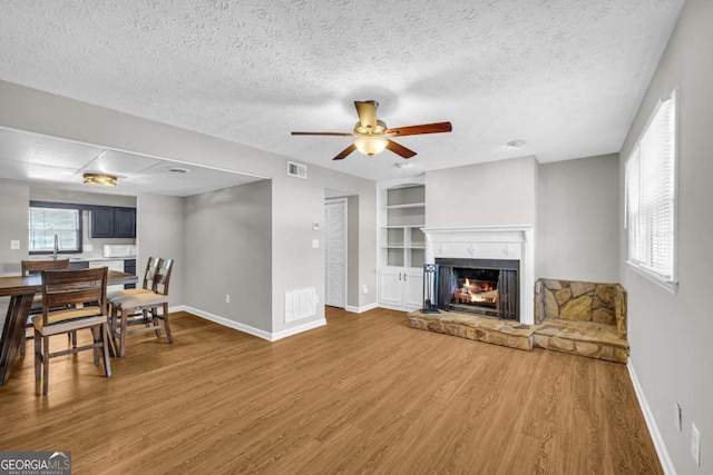 living area with visible vents, a lit fireplace, baseboards, and wood finished floors