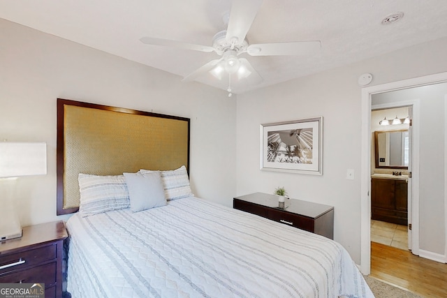 bedroom with light wood-type flooring, a ceiling fan, and ensuite bathroom