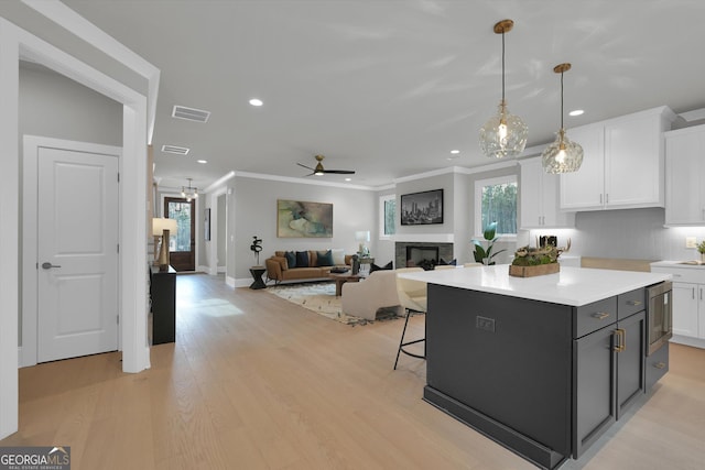 kitchen featuring light wood finished floors, visible vents, white cabinets, crown molding, and a fireplace