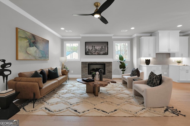 living room with ornamental molding, a fireplace, visible vents, and light wood-style floors