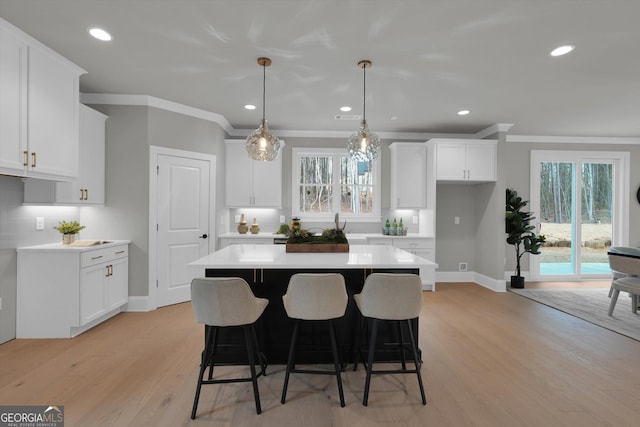 kitchen featuring a center island, light countertops, crown molding, light wood-type flooring, and white cabinetry