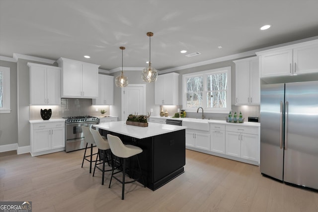 kitchen featuring stainless steel appliances, white cabinetry, light countertops, a center island, and crown molding