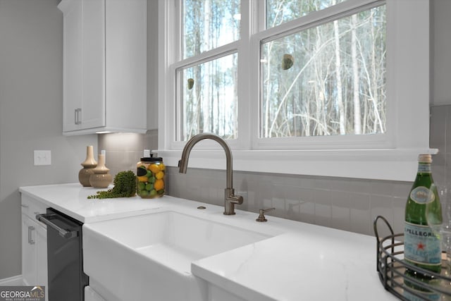 interior details featuring white cabinets, dishwasher, a sink, and light stone countertops