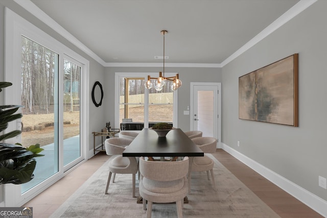 dining area featuring a notable chandelier, crown molding, light wood finished floors, visible vents, and baseboards