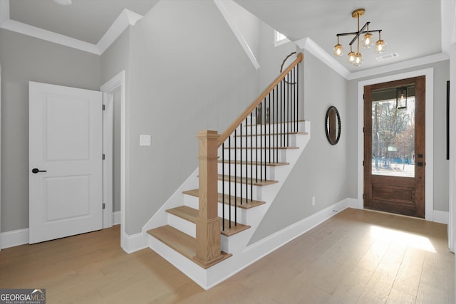 entryway with baseboards, wood finished floors, visible vents, and crown molding