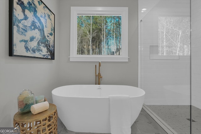 full bath with marble finish floor, a freestanding bath, and tiled shower