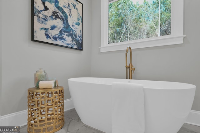 bathroom with a soaking tub, marble finish floor, and baseboards