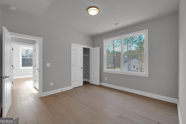 unfurnished bedroom with a closet, visible vents, baseboards, and wood finished floors