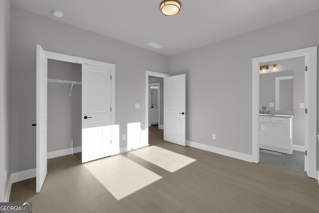 unfurnished bedroom featuring a closet, a sink, baseboards, and wood finished floors