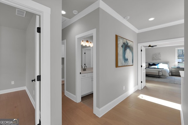 hallway with light wood finished floors, a sink, and visible vents