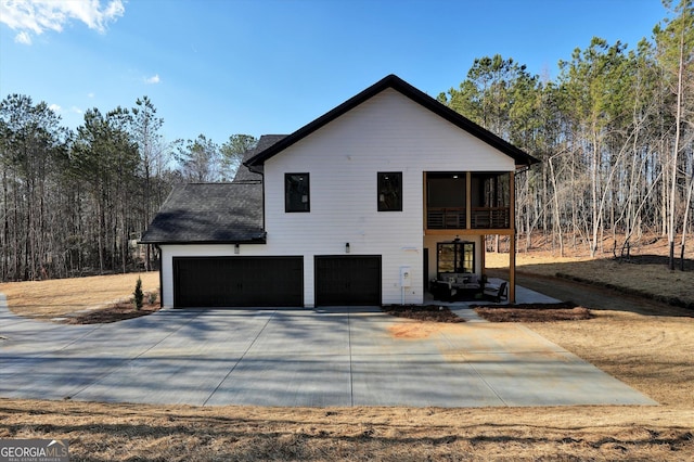 view of side of home with concrete driveway, roof with shingles, and an attached garage