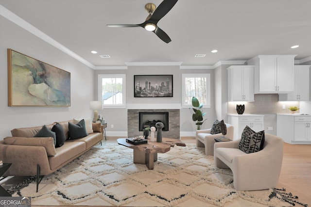 living room featuring a wealth of natural light, a fireplace, crown molding, and light wood-style flooring