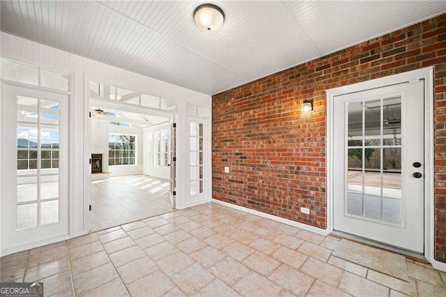 unfurnished room featuring stone tile flooring, a fireplace, and brick wall