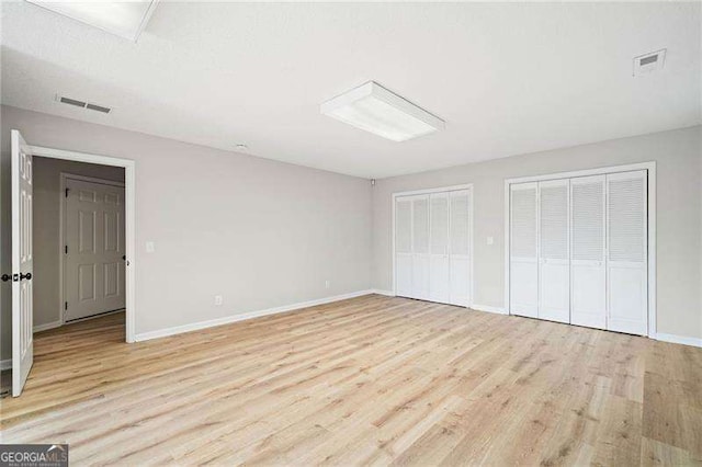 unfurnished bedroom featuring light wood-style floors, baseboards, visible vents, and two closets