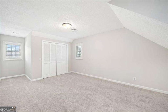 unfurnished bedroom featuring a closet, visible vents, light carpet, vaulted ceiling, and baseboards