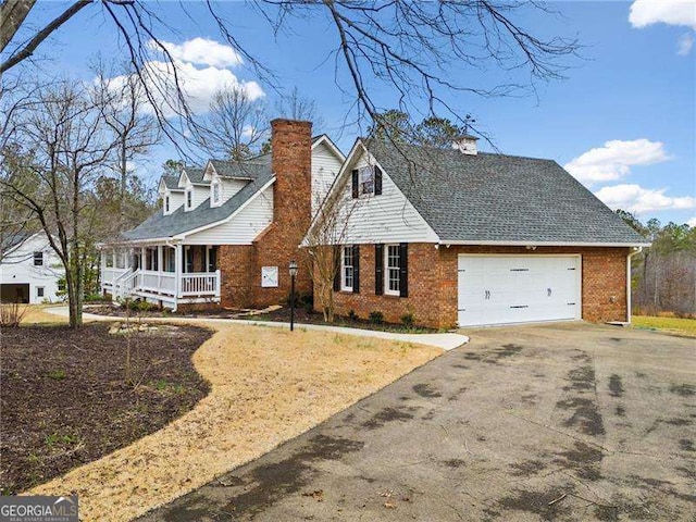 cape cod home featuring aphalt driveway, an attached garage, covered porch, brick siding, and a chimney