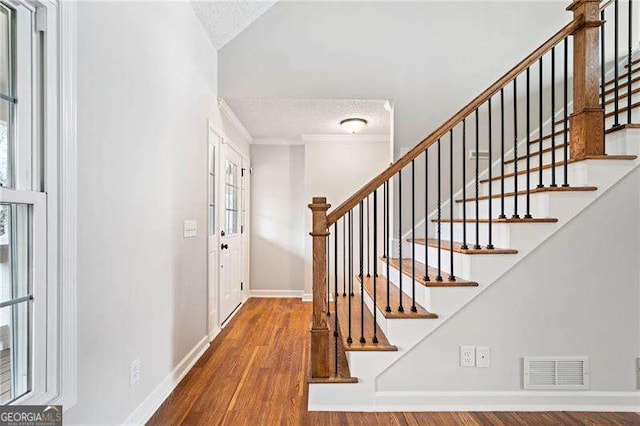 foyer featuring visible vents, ornamental molding, a textured ceiling, wood finished floors, and baseboards