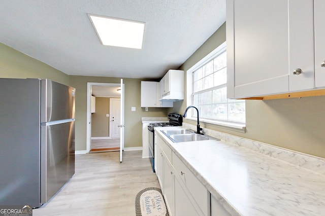 kitchen with light countertops, electric range, freestanding refrigerator, white cabinetry, and a sink