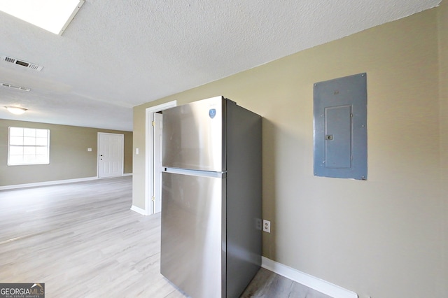 kitchen with a textured ceiling, baseboards, freestanding refrigerator, electric panel, and light wood finished floors