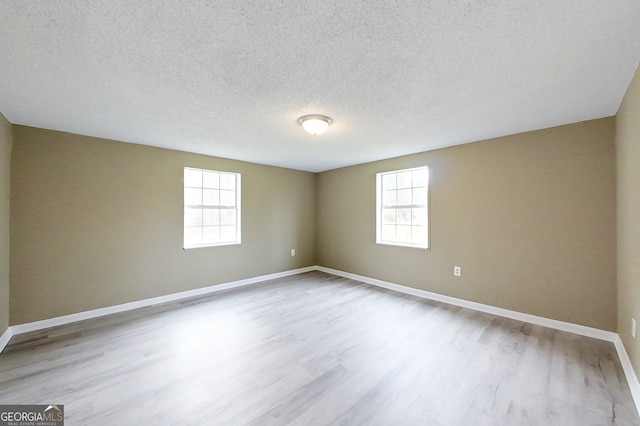 empty room with light wood-type flooring, a textured ceiling, baseboards, and a wealth of natural light