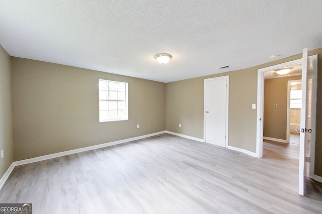 unfurnished bedroom with light wood-style floors, visible vents, a textured ceiling, and baseboards