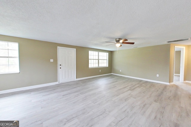 unfurnished room with light wood-style flooring, a textured ceiling, visible vents, and baseboards