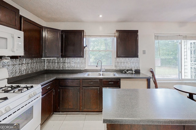 kitchen featuring dark countertops, decorative backsplash, dark brown cabinetry, a sink, and white appliances