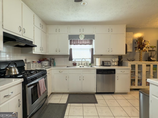 kitchen featuring light tile patterned floors, appliances with stainless steel finishes, a sink, under cabinet range hood, and backsplash