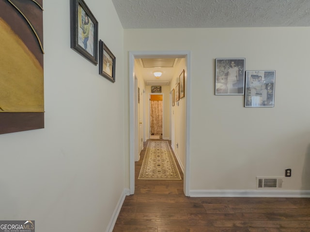 hallway with a textured ceiling, wood finished floors, visible vents, and baseboards