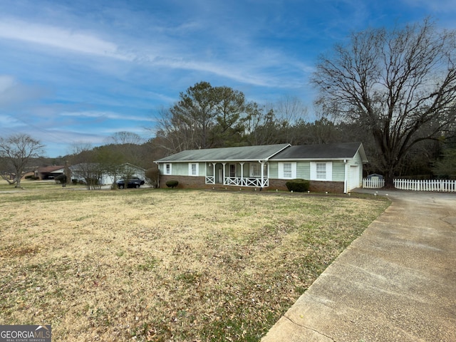 ranch-style home with concrete driveway, covered porch, fence, a front yard, and brick siding