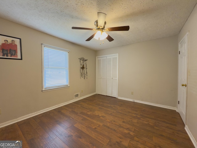 unfurnished bedroom with baseboards, a textured ceiling, visible vents, and dark wood-style flooring