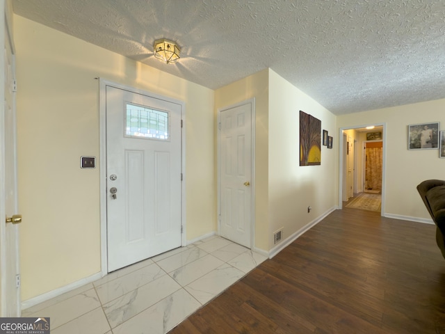 foyer featuring marble finish floor, baseboards, visible vents, and a textured ceiling