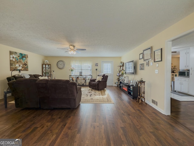 living room with baseboards, visible vents, a ceiling fan, dark wood-type flooring, and a textured ceiling