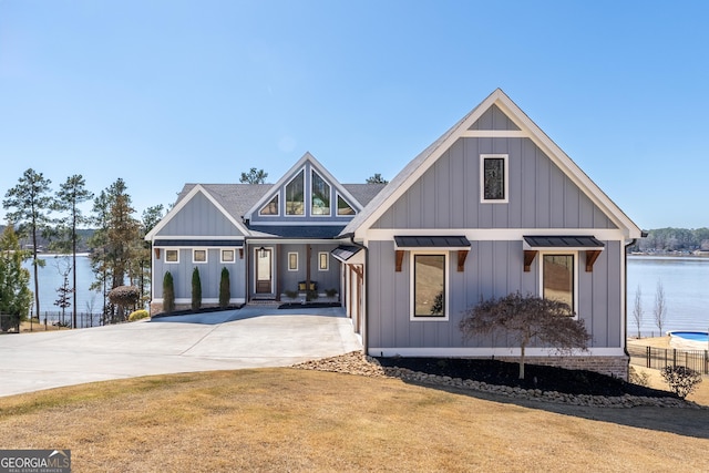 modern farmhouse with a shingled roof, concrete driveway, a water view, board and batten siding, and a front yard