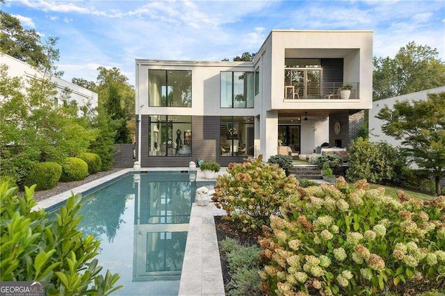 rear view of property featuring a balcony, an outdoor pool, and stucco siding