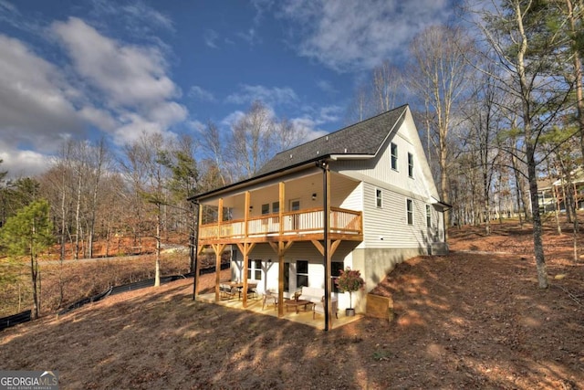 view of front of house with a deck, dirt driveway, roof with shingles, and a patio area