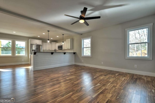 unfurnished living room with a healthy amount of sunlight, dark wood finished floors, and baseboards