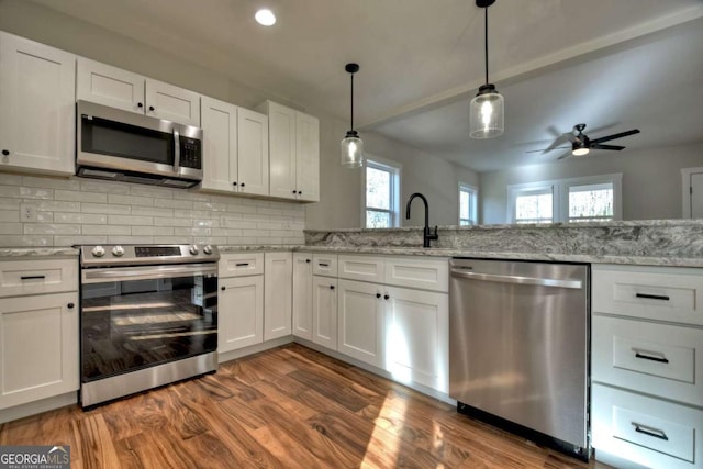 kitchen featuring white cabinetry, appliances with stainless steel finishes, backsplash, light stone countertops, and pendant lighting