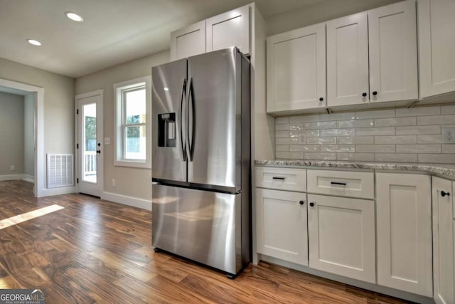 kitchen featuring light stone counters, visible vents, backsplash, white cabinets, and stainless steel fridge with ice dispenser