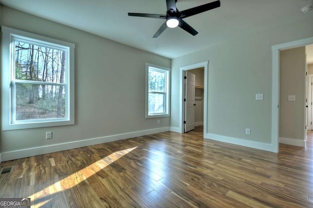 unfurnished bedroom featuring dark wood finished floors, a spacious closet, baseboards, and ceiling fan