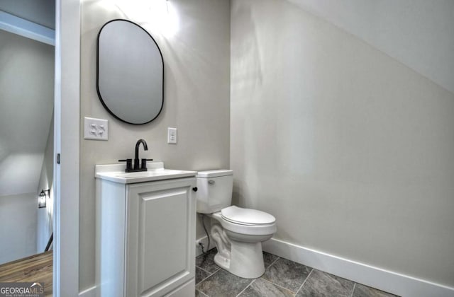 half bath featuring vanity, toilet, and baseboards