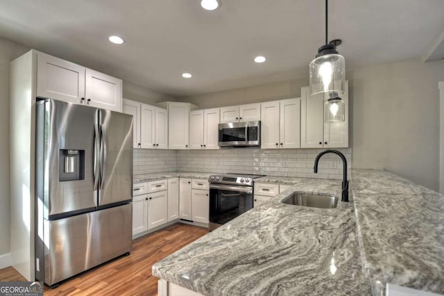 kitchen featuring appliances with stainless steel finishes, a peninsula, light stone countertops, white cabinetry, and a sink