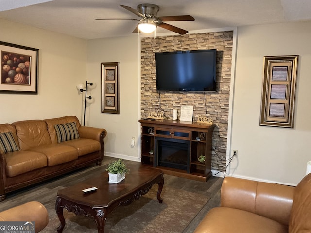 living room featuring dark wood-style flooring, a glass covered fireplace, a ceiling fan, and baseboards