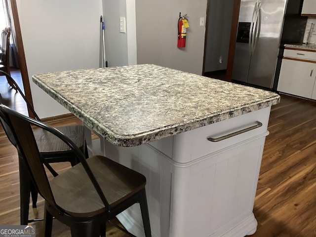 kitchen with light stone counters, a breakfast bar area, dark wood-style flooring, white cabinets, and stainless steel fridge