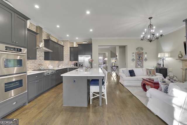 kitchen with stainless steel appliances, light countertops, open floor plan, a kitchen island with sink, and wall chimney exhaust hood