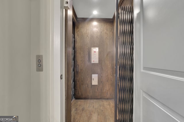 interior details featuring elevator, wood walls, and wood finished floors