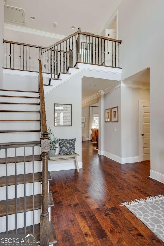 staircase featuring baseboards, a high ceiling, wood finished floors, and crown molding